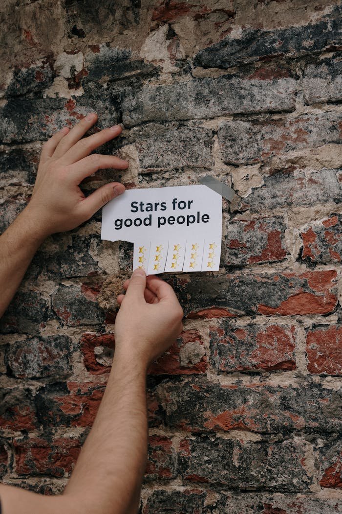 Close-up of hands taping a paper titled 'Stars for Good People' on a brick wall.